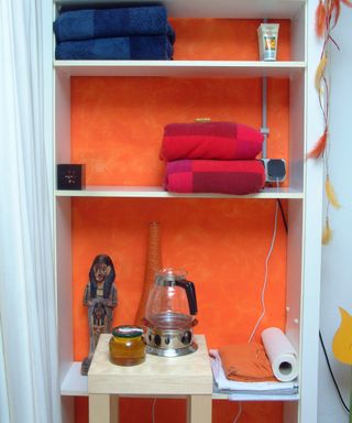 White shelves with orange wallpaper behind shelves