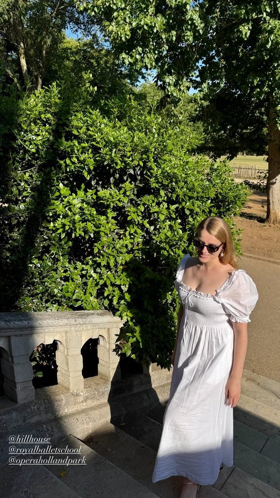 Flora Vesterberg wearing a white dress walking up a staircase with a tree in the background