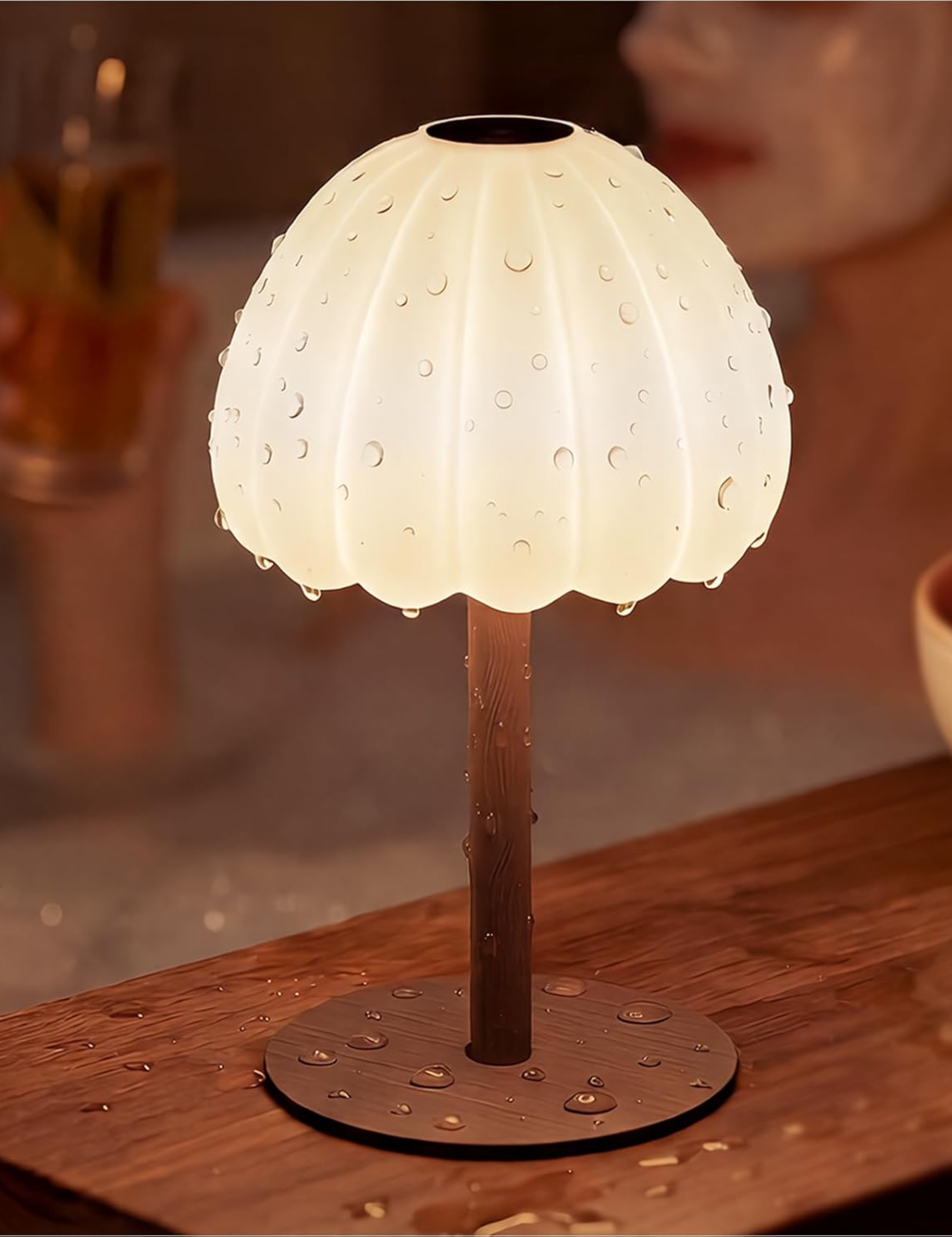 Fluted rechargeable lamp covered in water droplets sitting on a wooden tabletop
