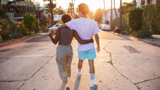 Young couple with their arms around each other walking down street - stock photo