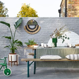 outdoor grey brick wall with wooden dinning table and bench and plant