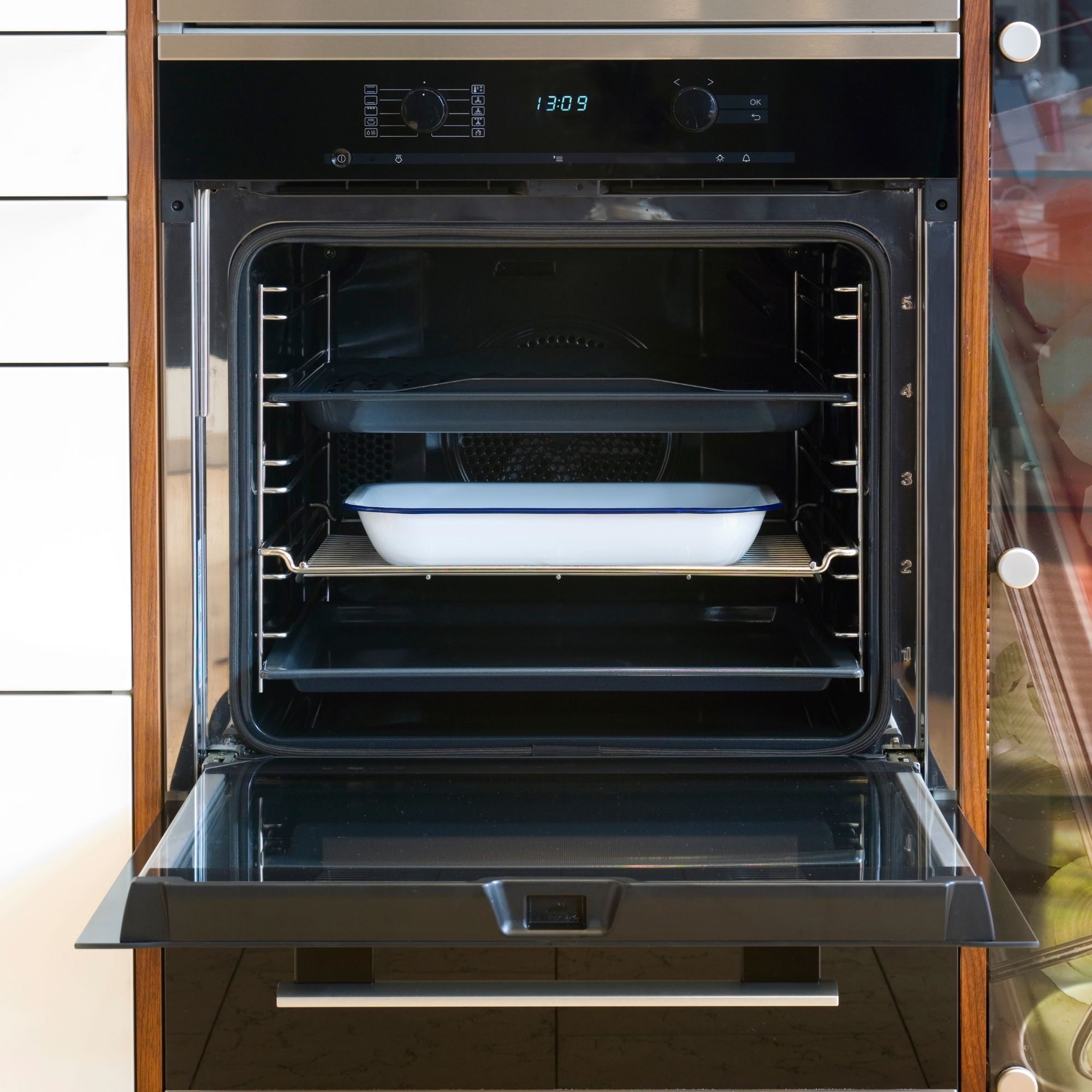 An oven with the door open and a white roasting tray inside of it