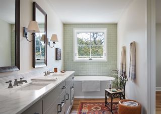 bathroom with pale green lustre tiles freestanding bath twin basins and traditional kilim rug and antique chair and wall mounted lamps