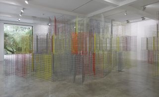 Rana Begum's gallery space, white walls, coloured mesh floor standing artwork, white ceiling with spotlights, window on the left wall with view of tree tops outside, grey gloss marble floor