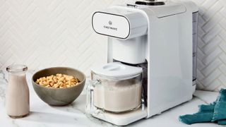 Chefwave Milkmade nut milk maker in white on a countertop next to a bowl of cereal and a milk carafe