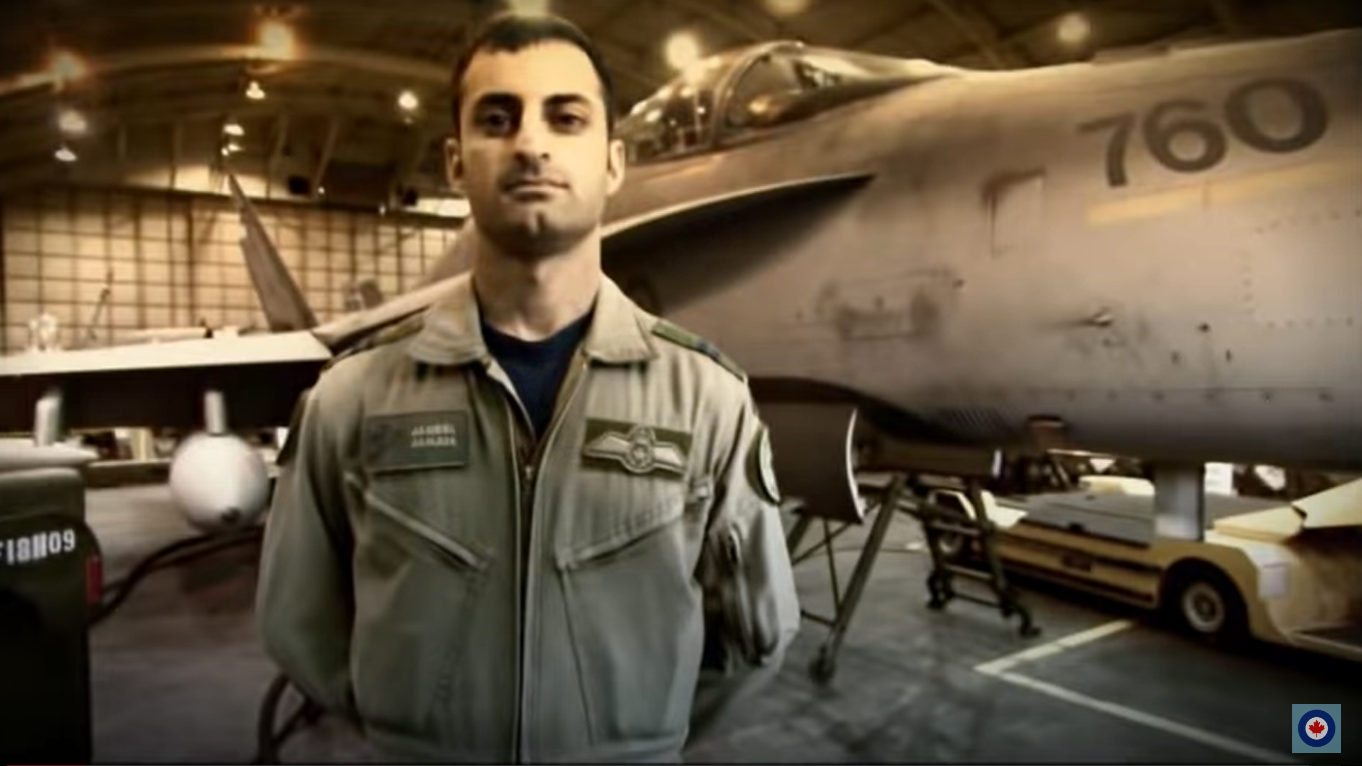 jameel janjua in a flight suit in front of a military airplane, in a hangar