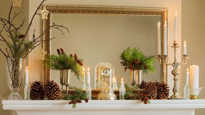 a mantel decorated for christmas with taper candles, foliage, and pine cones