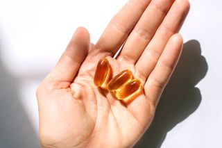 Probiotics for women: Woman's hand holding fish oil supplements on white background