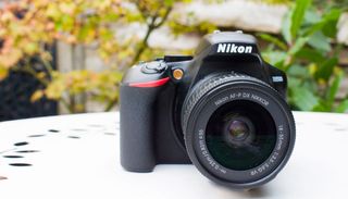 Nikon D3500 on a white table outside with green foliage behind