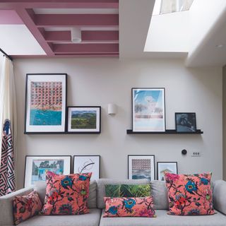 Living room with l-shaped sofa, prints on wall and painted pink beams.