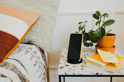 A nightstand next to a bed with an iPhone in a holder 