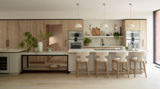 A light wood and off white kitchen with a long, multi level island with bar stools on one side and opposite the sink area and a walkthrough to a back kitchen or pantry