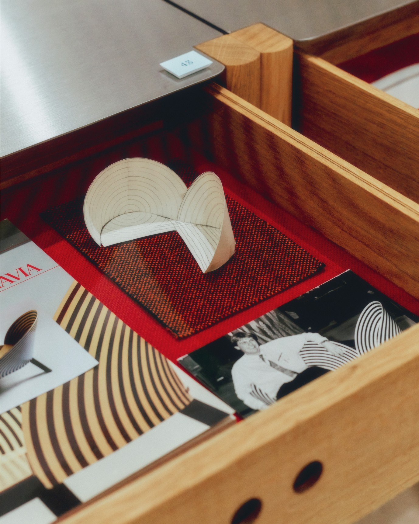 A wooden drawer filled with design memorabilia in red, black and white, and yellowed paper.