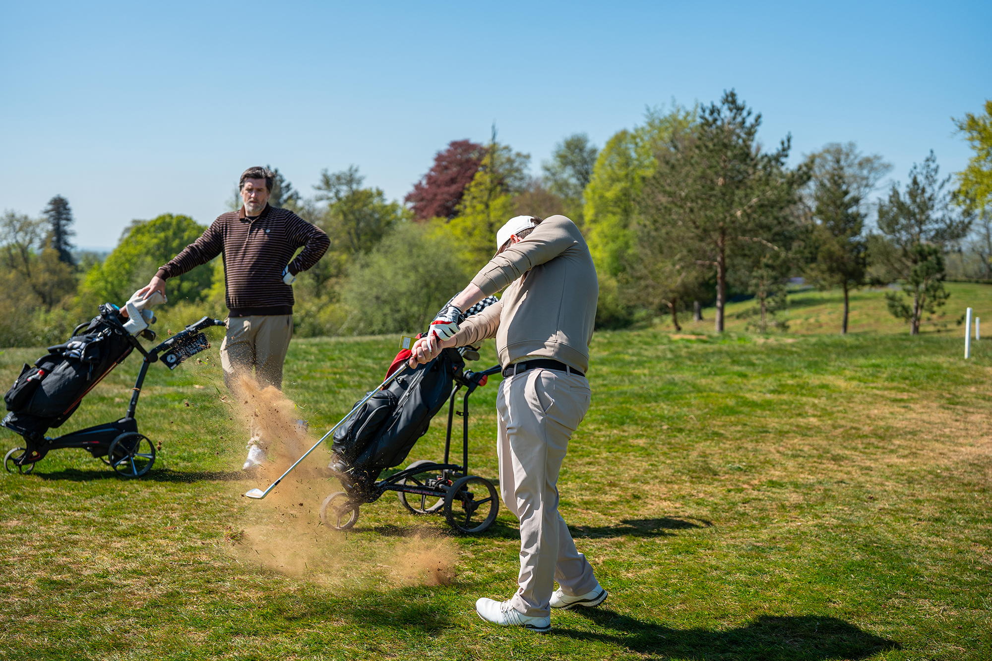 Elliott Heath hitting a shot on the fairway with Joe Ferguson watching