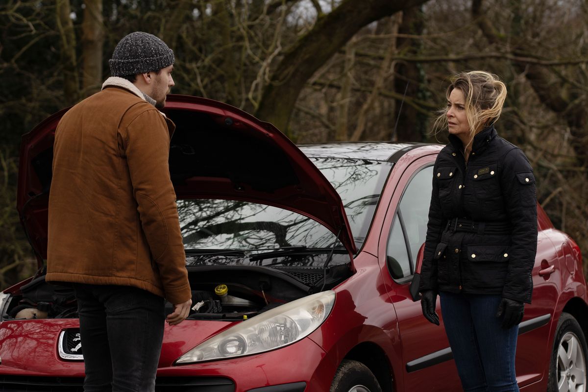 Charity and Mack talk by a car in Emmerdale.