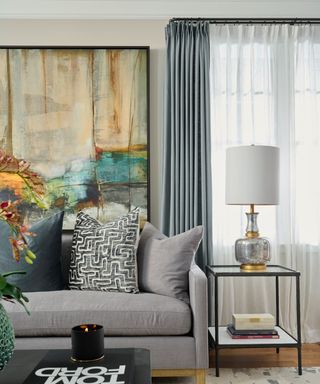 Living room with gray sofa, curtains and large artwork.