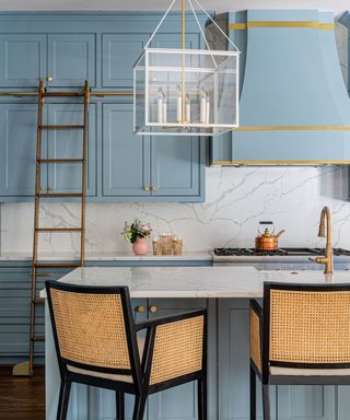 kitchen with light blue cabinets and island, marble countertops and rattan dining stools