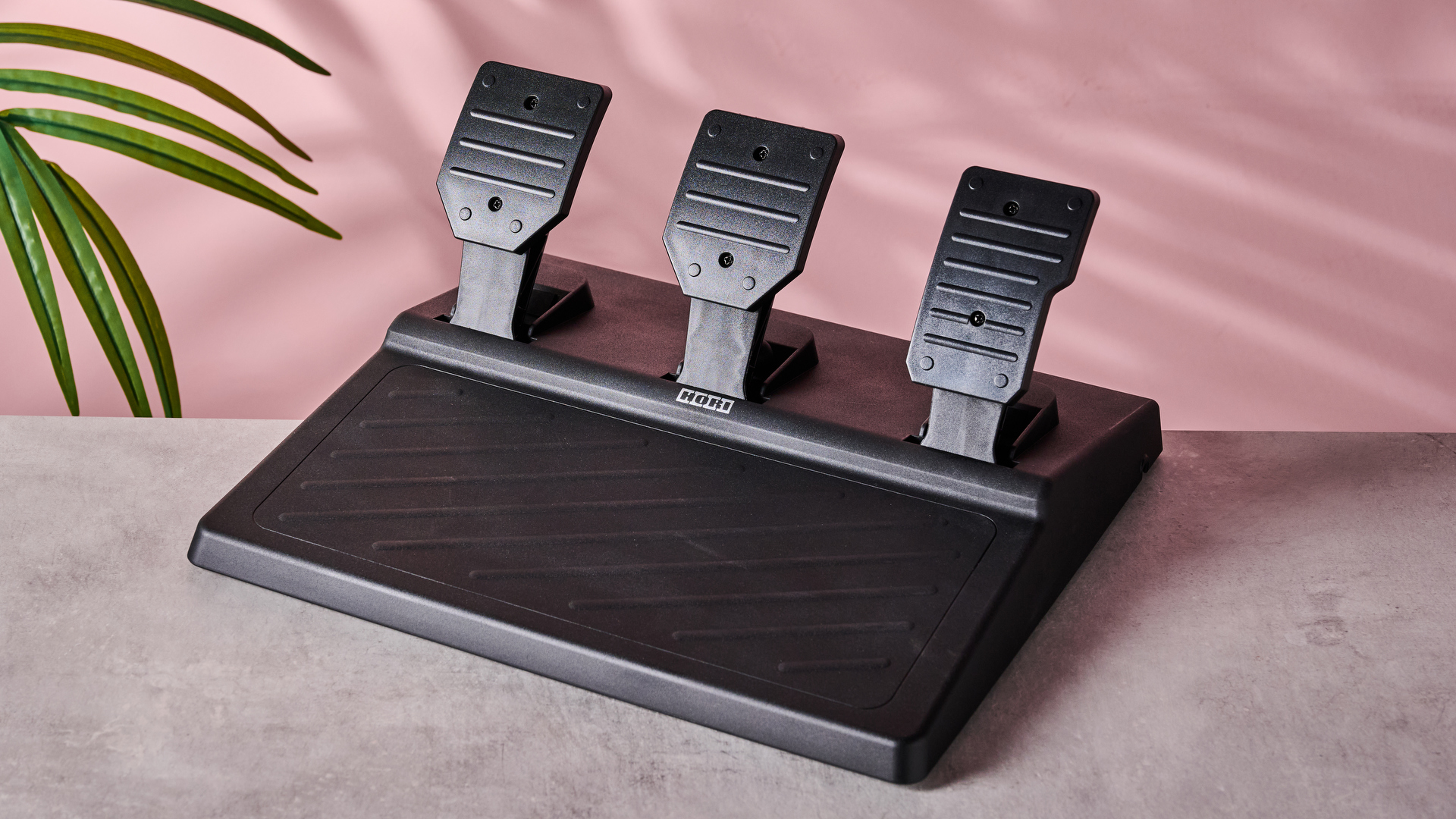 Pedal set for Hori Force Feedback Racing Wheel DLX, on desk with plant and pink wall in background