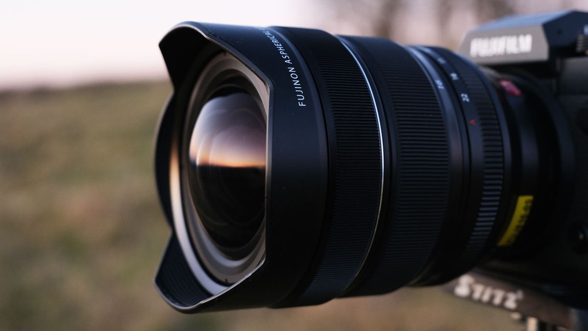 A side view of the Fujifilm X-H2 with the Fujifilm XF 8-16mm f/2.8 lens attached and a field in the background