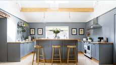 kitchen with gray blue cabinets wooden worktops and stools and pale stone flooring with beams and skylight