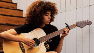 Lady plays acoustic guitar with a capo