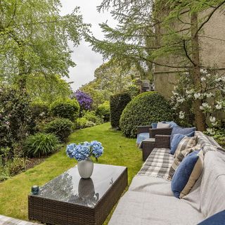 garden area with flower vase on glass table and sofa with cushions