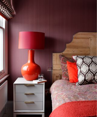 Textured bedroom wallpaper ideas in a red bedroom with wooden headboard and colorful prints.