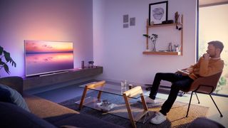 Philips TV's Ambilight glows around TV screen as man watches