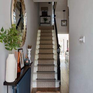 A narrow hallway with a white-painted staircase at the end covered with a beige stair runner