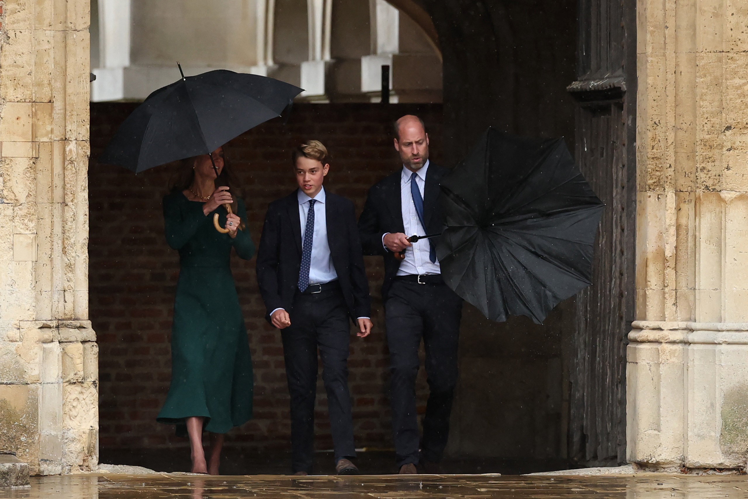 Prince William struggles with his umbrella walking next to Prince George and Princess Kate