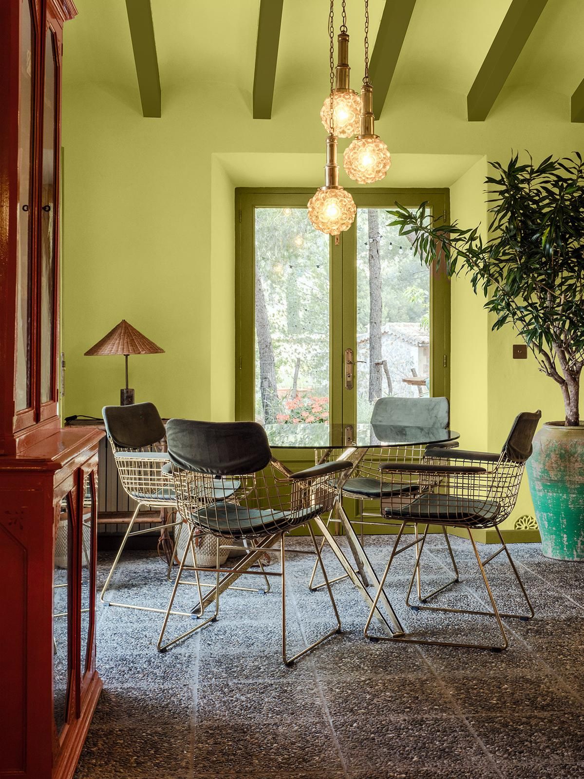 a green painted dining room with a round dining table and wire chairs