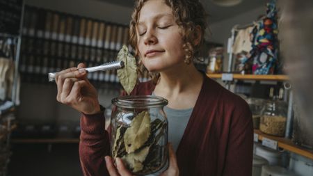 a photo of a woman holding up a bay leaf from a jar and smelling it