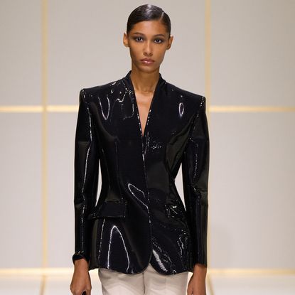 a model wears a shiny black jacket.