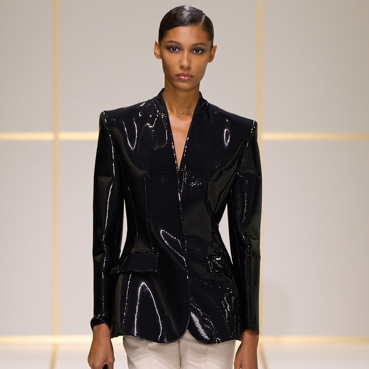 a model wears a shiny black jacket.