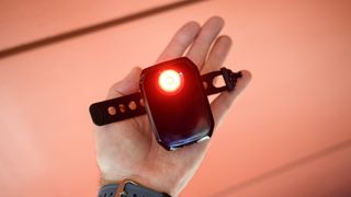 Trek CarBack Radar Rear Bike Light in someone's hand with the red light glowing brightly against an orange background.