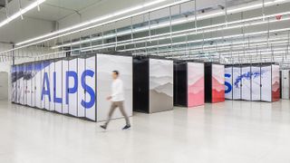 A photo of Alps supercomputer infrastructure in Lugano, Switzerland. A worker is blurrily walking in front of HPE supercomputer stacks which bear the words "Alps" in blue and an image of snowy mountain peaks.