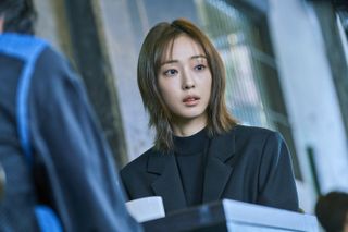 A woman (Jeon So-nee) looks shocked as she sits at a desk, in 'As You Stood By.'