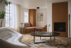 a modern living room with a round patterned rug, round coffee table, window seat, fireplace and striped table with a white sofa
