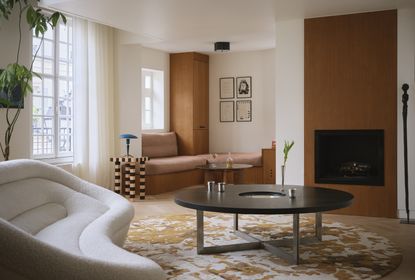 a modern living room with a round patterned rug, round coffee table, window seat, fireplace and striped table with a white sofa