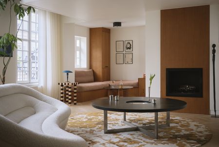 a modern living room with a round patterned rug, round coffee table, window seat, fireplace and striped table with a white sofa