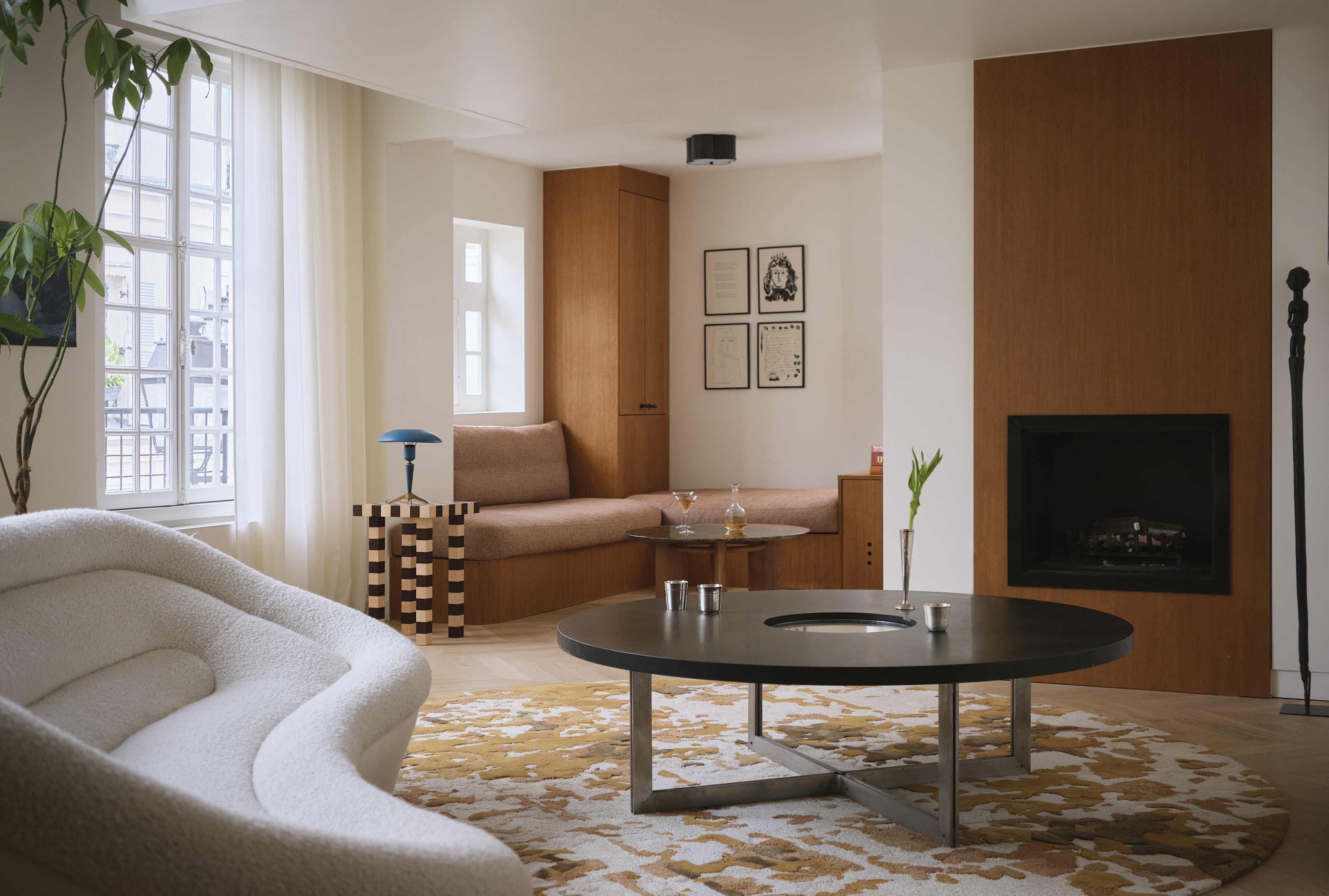 a modern living room with a round patterned rug, round coffee table, window seat, fireplace and striped table with a white sofa