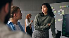 Male and female data engineers discussing strategy and work activities in an office space with sticky notes on a wall in the background.