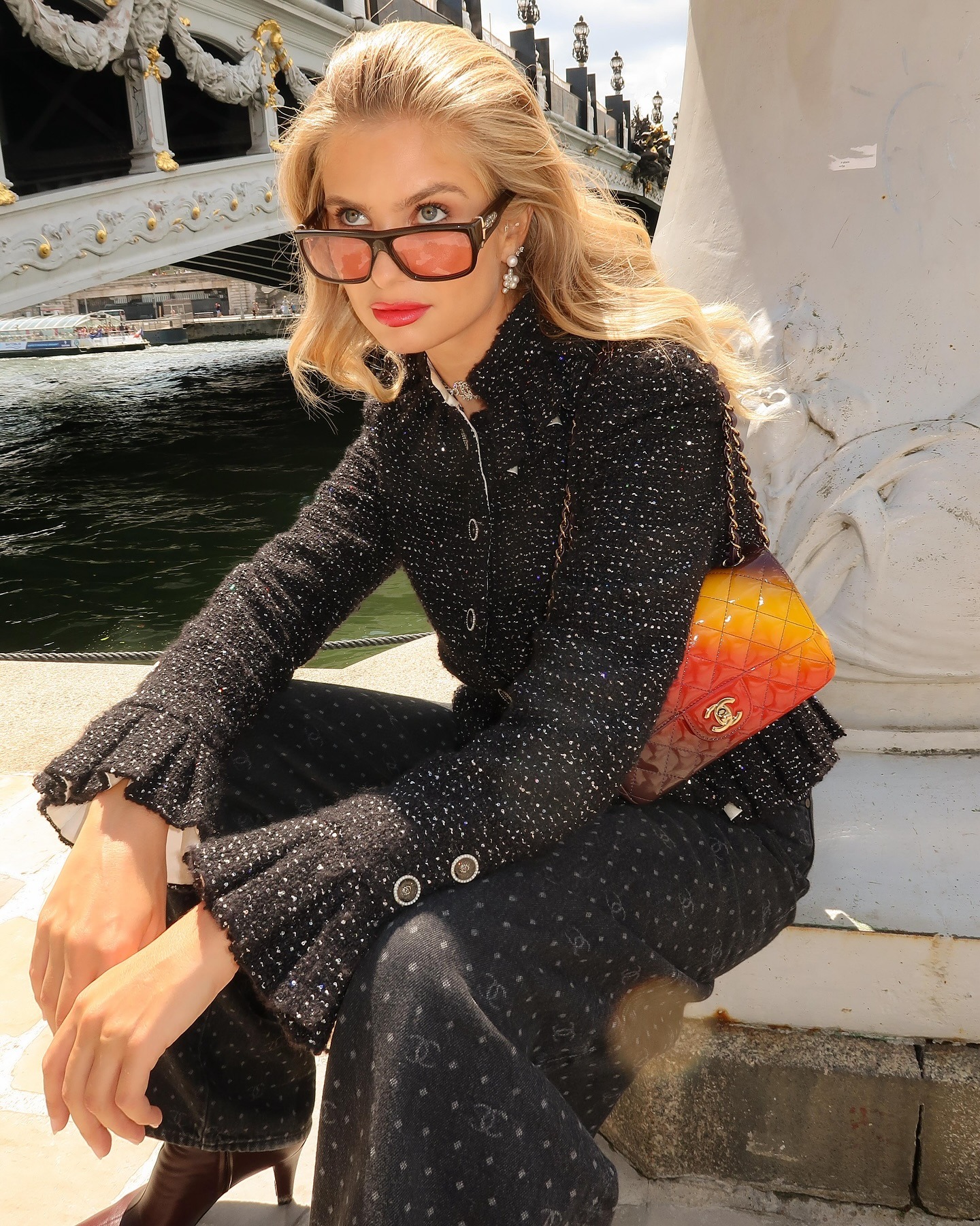 Xenia Donts wears the best autumn jacket in Boucle. She pairs it with black denim jeans, an orange ombree Chanel bag and sunglasses. She is sitting, looking away from the camera in a recent image from her Instagram.