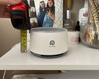 Dreamegg D1 white noise machine in white on nightstand, with measuring tape beside it to show the size