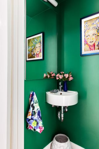 A bathroom painted deep green shade with a corner sink and colorful towel and picture