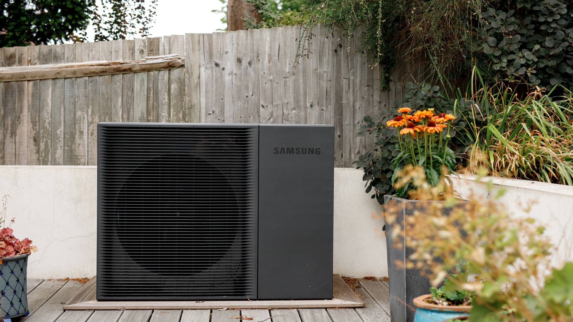 black heat pump mounted on decked area in garden
