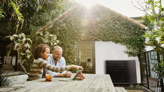 A father and daughter in the back garden with a heat pump connected to a house in the background