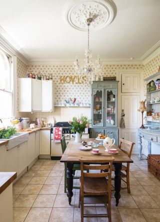 a big traditional kitchen with white units, two blue freestanding dressers, a large wooden dining table in the middle and a beige tiled floor