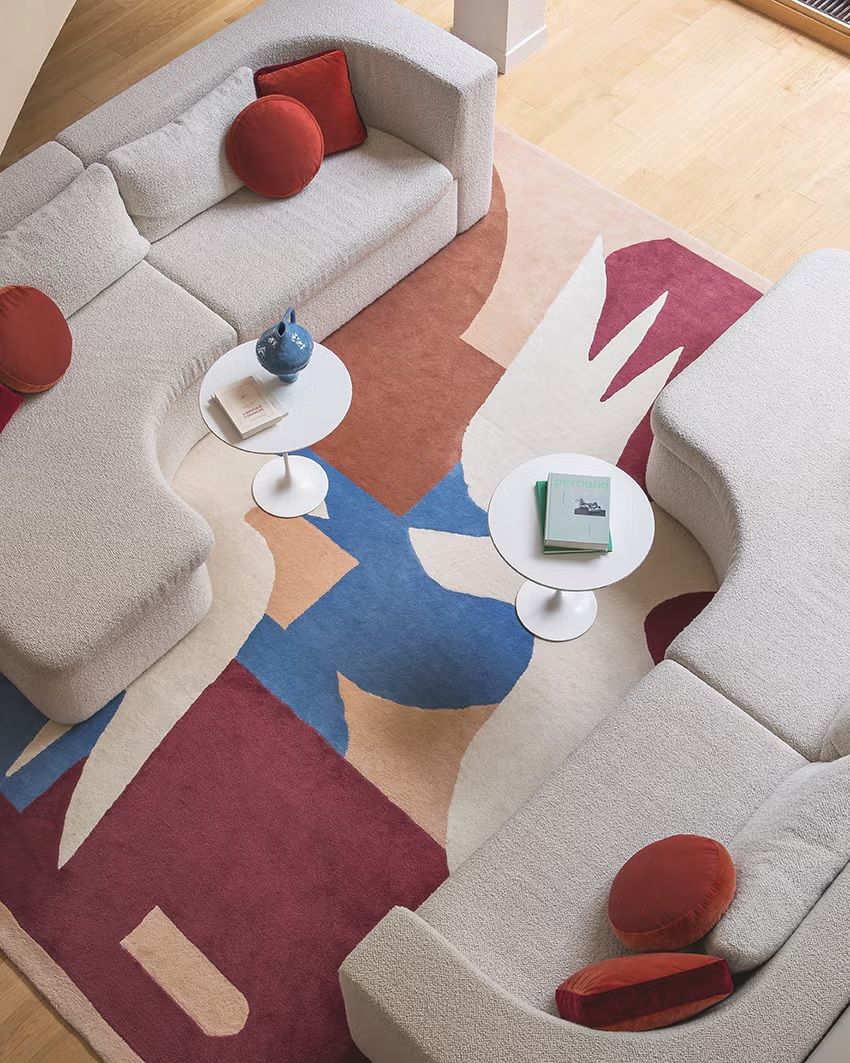 A lively decorated living room features colorful rugs, geometrically cut light brown sofas, and wooden floors.