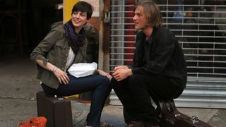 Anne Hathaway sitting on a suitcase on the side walk in 'Song One'